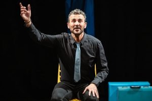 Un acteur expressif participant à un cours de théâtre parisien, assis sur une chaise et gesticulant