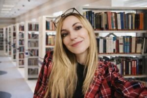 Portrait de l'autrice Céline Estelle souriante dans une bibliothèque pour son livre l’été Gigi.
