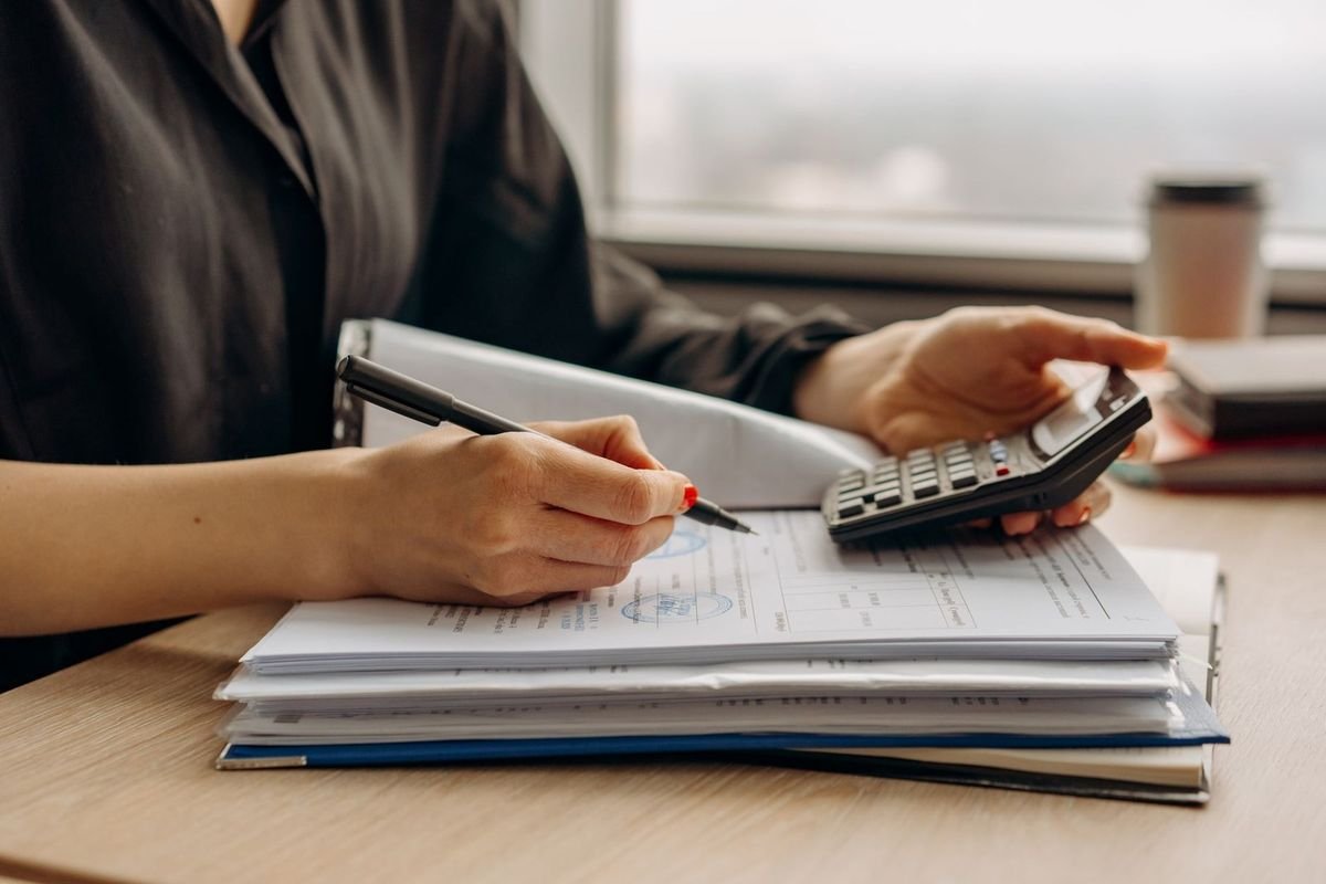 Individu prenant des notes avec une calculatrice sur une table près d'une fenêtre Individu prenant des notes avec une calculatrice sur une table près d'une fenêtre