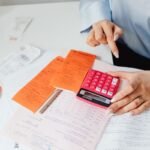 Une main sur une calculatrice, des papiers et des enveloppes sur une table