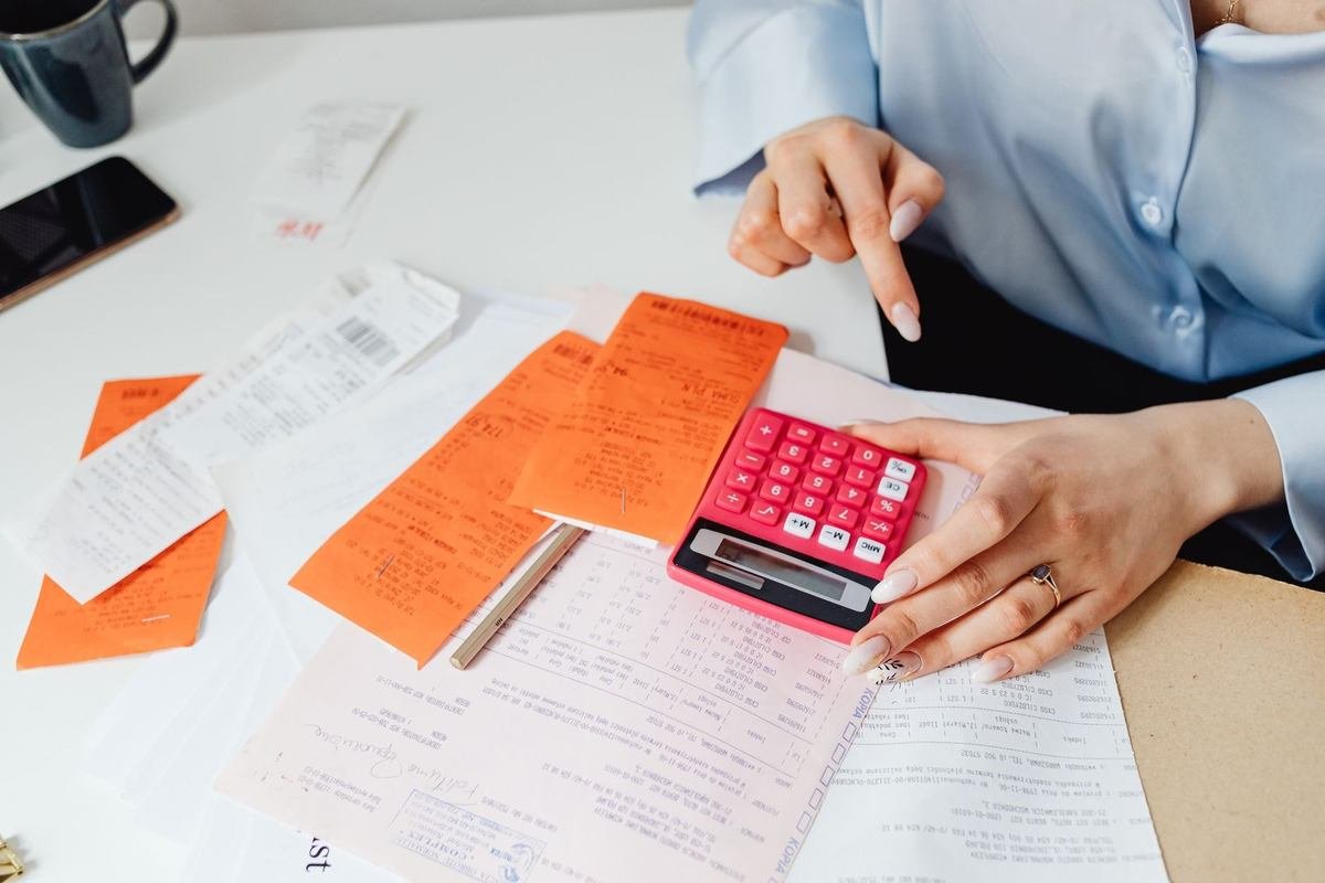 Une main sur une calculatrice, des papiers et des enveloppes sur une table