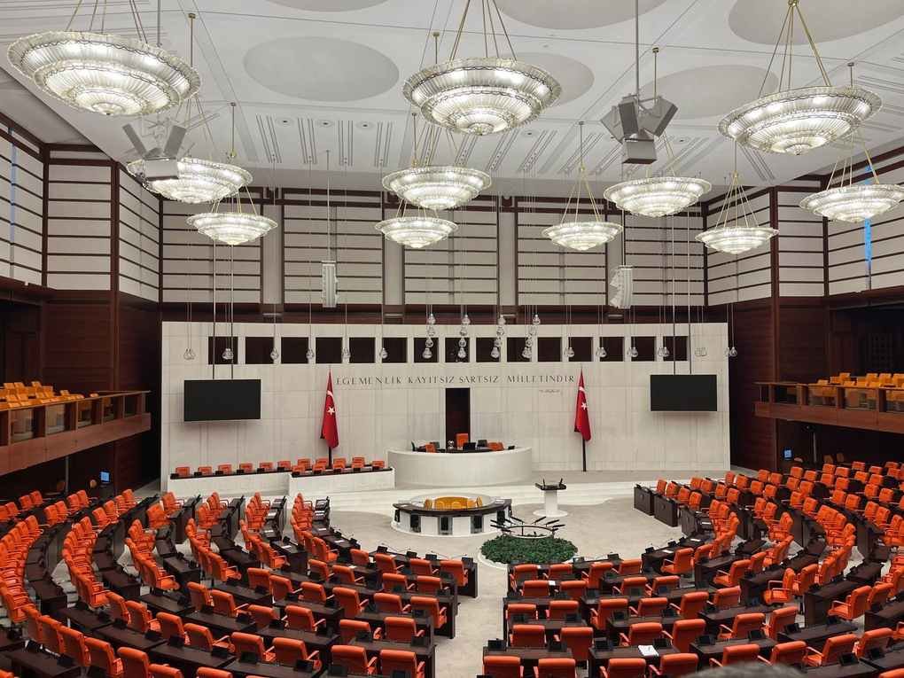 Salle de conférence avec amphithéâtre, sièges rouges, bureau central, drapeaux, écrans, éclairage suspendu Salle de conférence avec amphithéâtre, sièges rouges, bureau central, drapeaux, écrans, éclairage suspendu