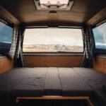 Intérieur d'un véhicule camper avec lit pliant, rideaux et vue extérieure