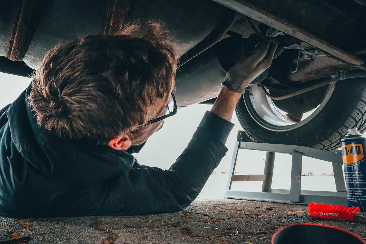 Homme sous un véhicule, manipulant la suspension avec des outils à proximité Homme sous un véhicule, manipulant la suspension avec des outils à proximité