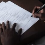 Mains noires écrivant sur un papier avec un stylo sur une table