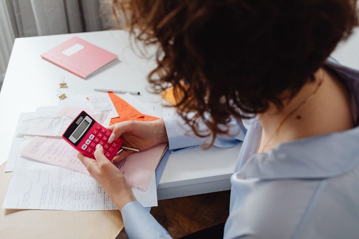 Femme utilisant une calculatrice rouge sur un bureau avec des documents et un agenda rose