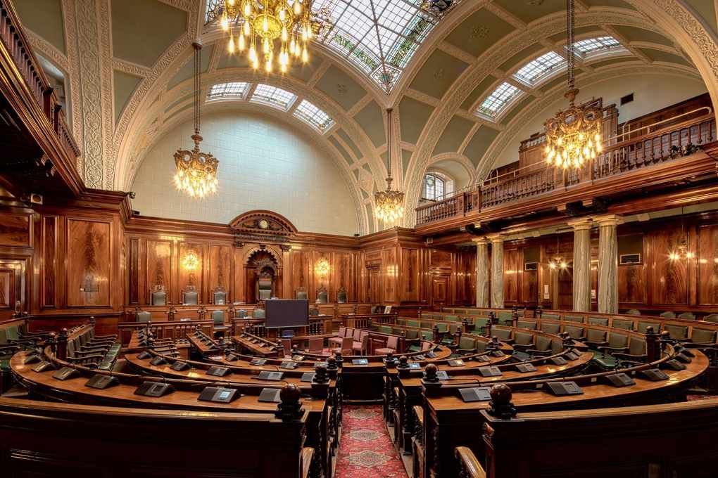 Salle parlementaire avec bureaux courbes, chandeliers, balcons, et vitraux