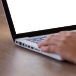 Personne utilisant un ordinateur portable avec écran blanc sur bureau en bois, vue de côté