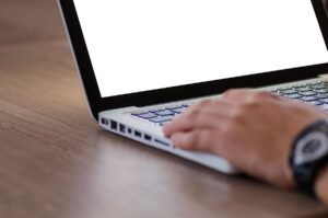 Personne utilisant un ordinateur portable avec écran blanc sur bureau en bois, vue de côté