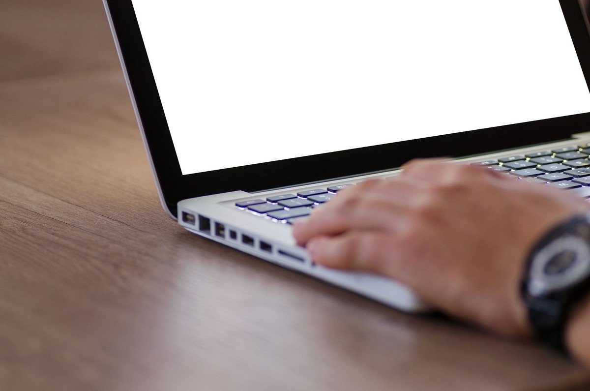Personne utilisant un ordinateur portable avec écran blanc sur bureau en bois, vue de côté